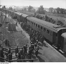 A black and white photo of numerous men, some carrying backpacks, heading for a train.