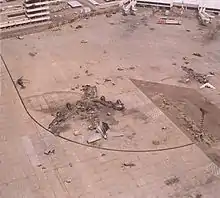 Wreckage in outline of burned-out aircraft; only the tail assembly is intact