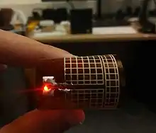 A printed rectenna lighting an LED from a Powercast 915&nbsp;MHz transmitter, flexible meshed antenna bent with a red LED light
