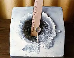 A 7-gram object (shown in centre) shot at 7&nbsp;km/s (23,000&nbsp;ft/s), the orbital velocity of the ISS, made this 15&nbsp;cm (5.9&nbsp;in) crater in a solid block of aluminium