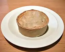 A circular pie, about 8&nbsp;cm in diameter and 4&nbsp;cm high, on a dinner plate, with no accompaniments