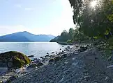 Plage de galets sur le lac avec des touristes (au fond).