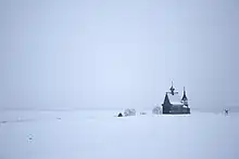 Photographie d'un paysage plat entièrement blanc, avec seulement une église en bois qui sort de ce paysage enneigé.