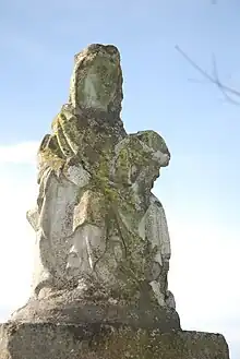 Statue d'une Vierge, couverte de mousse, sur fond de ciel bleu.