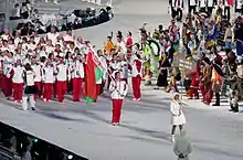 Un athlète en blanc et rouge tient le drapeau biélorusse puis un groupe d'athlètes biélorusses est derrière lui.