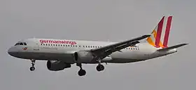 Photo du côté gauche d'un avion de ligne, aux couleurs blanches avec des bandes oranges et rouges sur la queue, en phase d'approche avec le train d'atterrissage sorti.