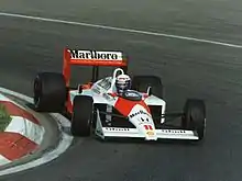 Photo d'Alain Prost au volant d'une McLaren MP4/4 en train d'engager un virage serré.