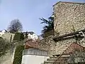 Hauts murs de pierres appareillées, parcourus par un escalier à rambarde en fer forgé.