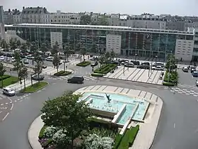 Photographie d'une gare de verre, un rond-point avec une fontaine au premier plan.