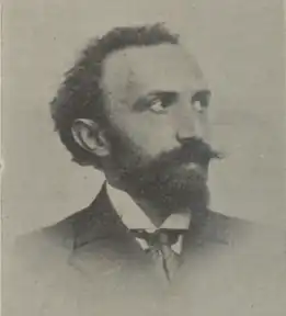 Portrait en noir et blanc d'un homme barbu portant un costume et une cravate.