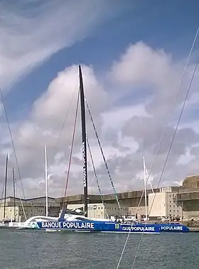 trimaran géant vu de profil légèrement arrière amarré devant un grand blockaus