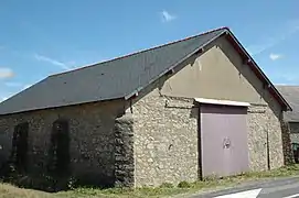 Vue d’un bâtiment en pierres, aux contreforts latéraux solides, et à la porte rouge.