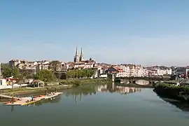 Vue d'un cours d'eau avec un pont à 3 arches, les flèches d'une cathédrale en arrière-plan.