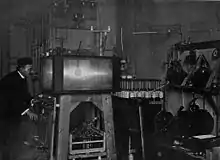 Photo ancienne en noir et blanc d'un homme penché vers une boîte transparente contenant une sphère.