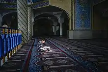 Assis en tailleur dans un rayon de lumière un jeune garçon lit un livre qu'il tient dans ses jambes. Le reste du lieu est vide, est la pièce, ses tapis, murs, piliers, couloirs, voutes, sont dans une quasi obscurité.