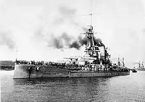 Un bateau de guerre dans un port, avec une foule de personnes sur le pont.