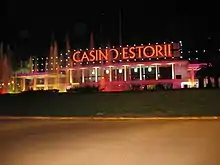 Photographie nocturne montrant un bâtiment alongé, où Casino Estoril est écrit en lettres rouges illuminées,