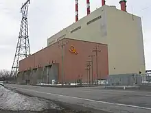 Arrière de la centrale de Tracy, un bâtiment industriel avec 4 cheminées. À gauche, on voit un gros pylône électrique.
