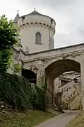 Photographie en couleurs d'une tour cylindrique couverte d'ardoises en arrière-plan d'un pont enjambant une rue encaissée.