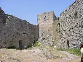 photo couleur montrant un château vu de la cour intérieure. Une tour, au fond, est reliée à deux murailles percées de trous montrant des emplacements de poutre anciens.