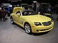 Une voiture cabriolet jaune 2 portes, coffre ouvert, vue de l'avant droit exposée dans un salon.