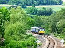 Un petit train circule sur une ligne de chemin de fer au milieu de la campagne.