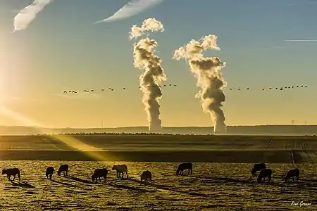 Photo prise depuis la Belgique de la vapeur sortant de la centrale nucléaire de Chooz avec également des trainées d'avions dans le ciel.