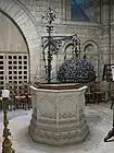 Photo : cuve de pierre sculptée surmontée de son couvercle en fer forgé avec potence.