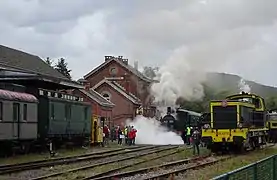 Festival Vapeur 2018 : Ambiance vapeur à Treignes. La locomotive a vapeur AD05 démarre en purgeant ses cylindres. La fumée d'une autre locomotive à vapeur est visible derrière la locomotive diesel BB 63.149.