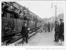 Photographie de plusieurs voitures remplies de conscrits en train de quitter le quai.