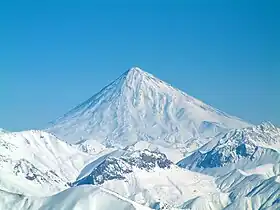 Volcan conique, enneigé, surmontant très largement des montagnes d'altitude plus modeste, bien qu'également enneigées.