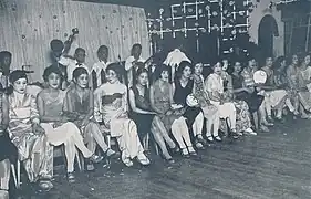Photo d'une salle de danse : des femmes sont alignées et assises sur des chaises, prêtes à aller danser.