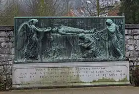 Surmonté d'un bas-relief en bronze, la scène représente un gisant qu'un ange vient coiffer d'une couronne. Un second personnage à droite tend également une couronne à la veuve éplorée tenant son enfant qui est agenouillée au pied du défunt. Le socle mentionne le souvenir dinantais aux 674 victimes innocentes de la furie teutonne dont 116 trouvèrent la mort ici.