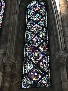 Vitrail composé de pièces rectangulaires et triangulaires. Sont représentés différents personnages dans plusieurs scénettes, difficilement visibles en raison du noircissement du vitrail.