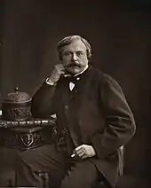 Portrait photographique d'un homme portant une moustache, se tenant assis, le coude posé sur une table et l'avant-bras soutenant sa tête.