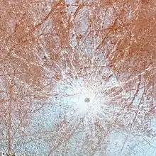 Zoom sur le cratère. Un petit point brun est visible, entouré de lignes blanches partant dans toutes les directions depuis celui-ci.