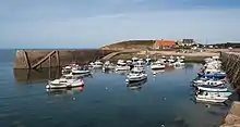 Vue d'un petit port à marée haute. Une jetée sur la gauche, une quarantaine de petits bateaux de pêche et de plaisance au mouillage.