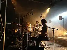 Photographie en couleurs d'un groupe de musiciens en représentation, sur une estrade, un batteur étant au premier plan.