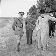 Sur fond de paysage de campagne, le général Montgomery (âgé d'une cinquantaine d'années, en uniforme) et Winston Churchill (une soixantaine d'années, en civil) entourent Pierre II (âgé d'environ 18&nbsp;ans, en uniforme).