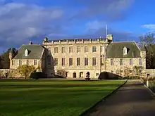 Photo en couleurs d'un bâtiment flanqué de deux ailes massives de teinte gris clair sous un ciel bleu.