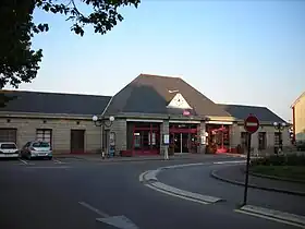 Photographie en couleurs d’un bâtiment marron, la gare ferroviaire d’Alençon, avec un ciel bleu au-dessus et des arbres.