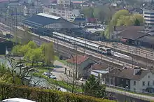 Gare au milieu de la ville sur une voie ferrée avec une verrière surplombant les quais, les voies et un train.