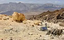 Petit boitier métallique au milieu de roches jaunâtres.