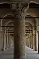 Une colonne à fût en marbre veiné et à chapiteau corinthien du portique occidental. En arrière-plan, l'alignement symétrique des arcades.