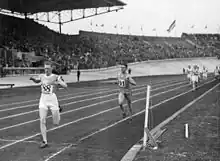 Photographie en noir et blanc de l’arrivée d'une course à pied dans un stade à huit clos.