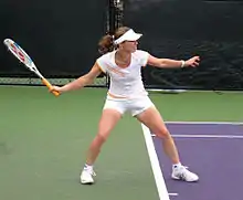 Photographie couleur d'une femme, de profil, préparant son coup droit, la tête tournée vers la droite