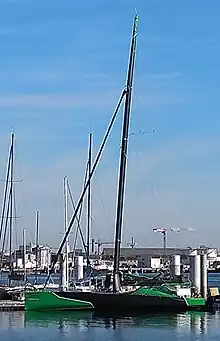 En entier de profil, voilier vert et noir amarré au ponton.