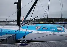 Voilier bleu clair et blanc amarré au ponton. Vue latérale du milieu. Le pont est blanc. La superstructure (rouf et casquette) est bleue.