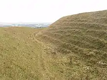 Grand fossé herbu avec une butte de terre de 3 ou 4 mètres à droite.