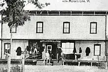 Une photographie ancienne d'un bâtiment portant les inscriptions «&nbsp;Canada », «&nbsp;J. M. Hill&nbsp;» et «&nbsp;U.S.A.&nbsp;».